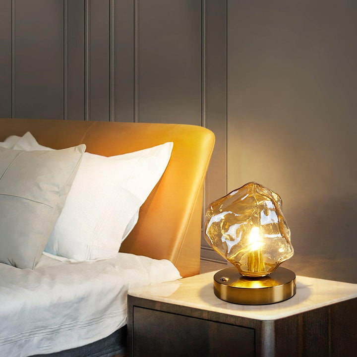 Szklana designerska lampa stołowa w kształcie bryły lodu na drewnianym blacie