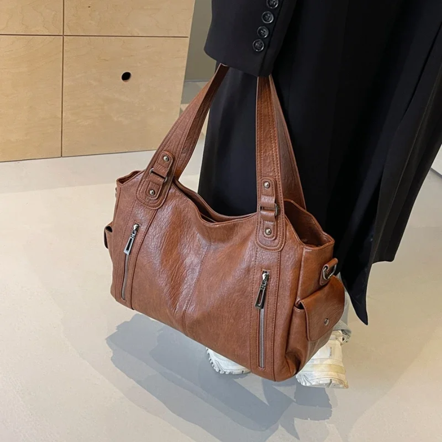 Torebka Amber na ramię w kolorze brązowym, wykonana z materiału roślinnego, z paskiem na ramię, metalowymi detalami i kieszeniami, elegancki i przestronny design dla kobiet.
