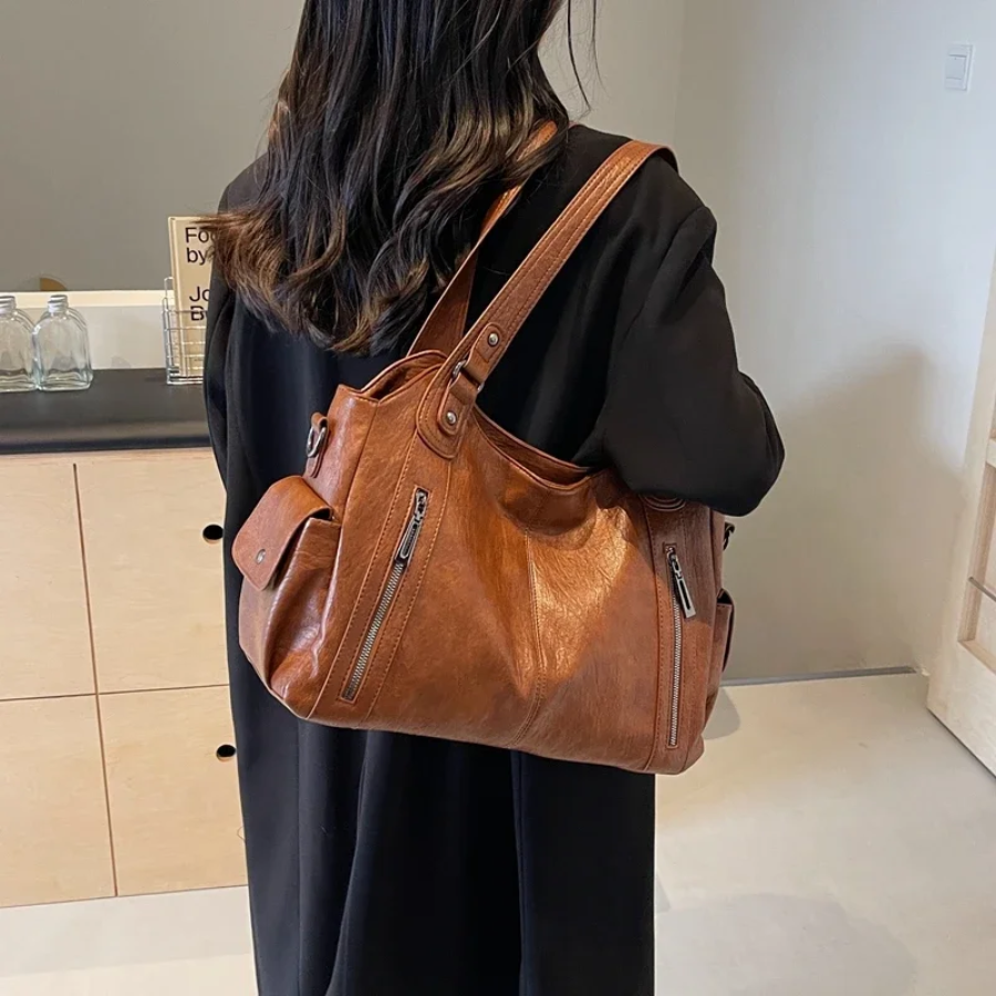 Torebka Amber na ramię w kolorze brązowym, wykonana z materiału roślinnego, z paskiem na ramię, metalowymi detalami i kieszeniami, elegancki i przestronny design dla kobiet.